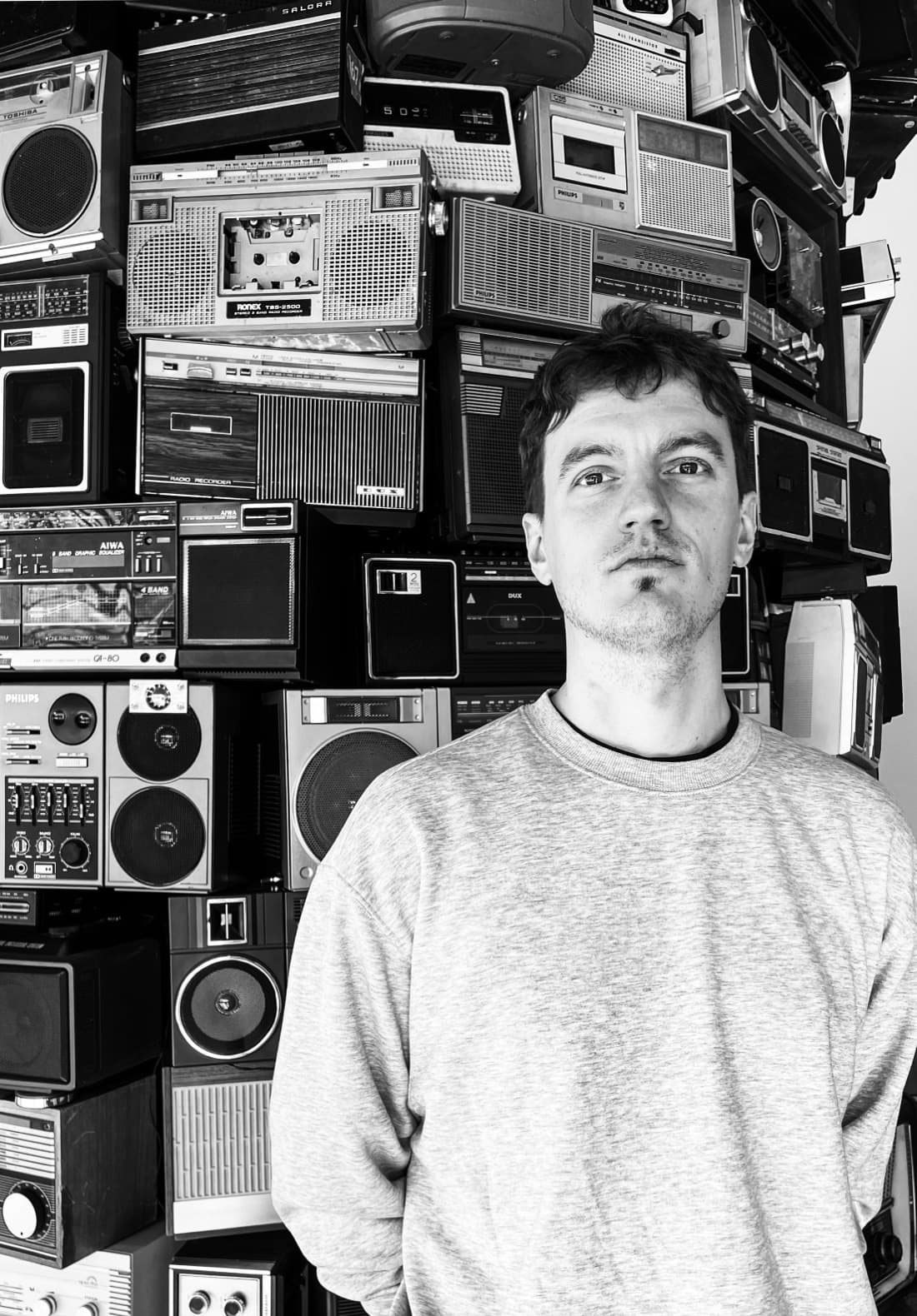 Fernando, founder of GrantGigs, in front of a wall of stacked vintage radios and boomboxes